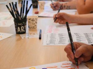 Personas practicando trazos y letras con rotuladores en un curso de lettering en Madrid