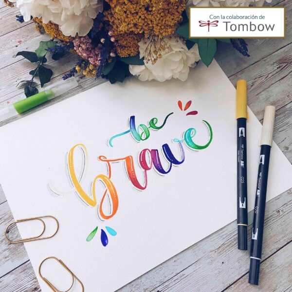 Lámina con lettering a color que dice ‘be brave’, decorada con rotuladores Tombow y flores secas en el fondo.